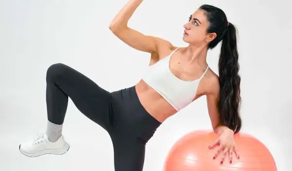 Frau macht Übungen mit Gymnastikball. Sie fragt sich, was ist Kreatin, während sie ihre Muskeln trainiert.